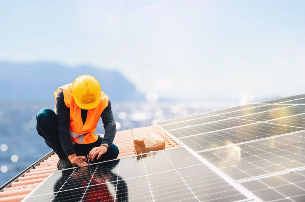 A solar installer works to install panels on to a roof overlooking a lake.